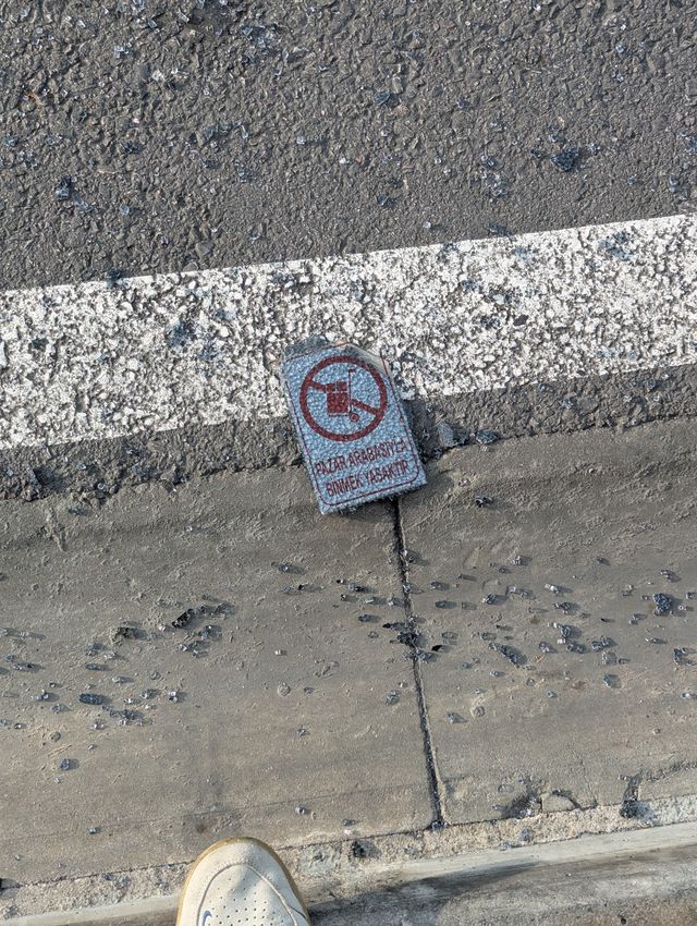 A broken piece of a sign lying on asphalt among shattered glass, displaying a 